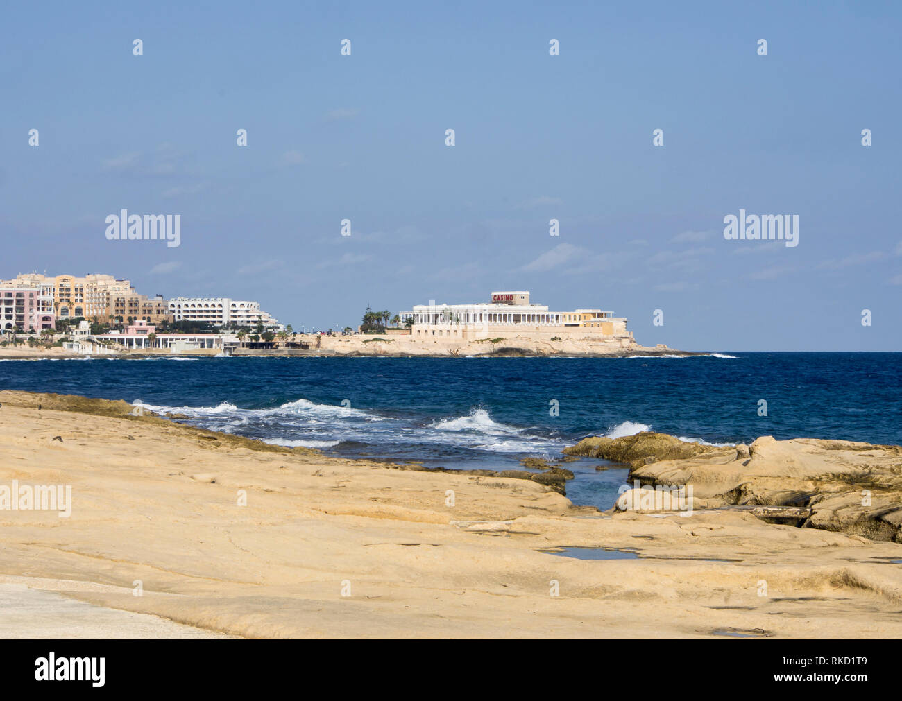 Blick entlang der Küste zu Fuß in Saint Julians Malta gegenüber dem Casino, herbstliche Sonne und Mittelmeer blaue Meer macht es zu einem beliebten Ferienziel Stockfoto