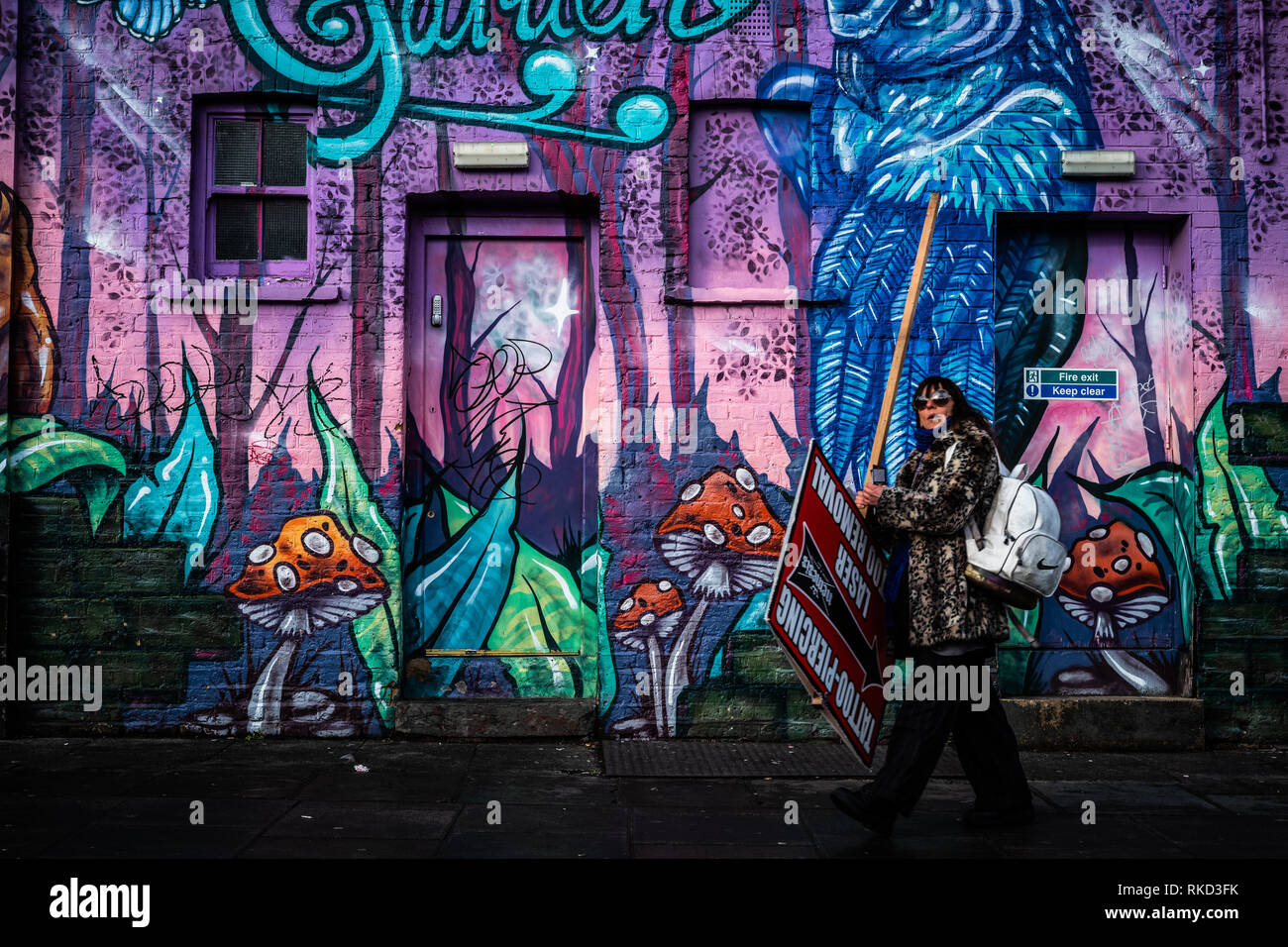 Lady witn großes Schild zu Fuß durch eine Wand mit Graffiti Kunst in Camden, London. Stockfoto