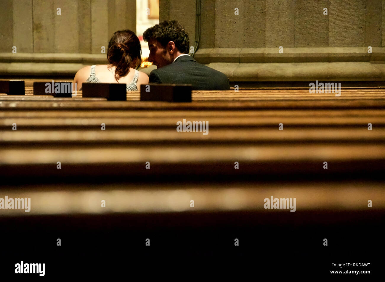 Ein Mann und eine Frau drängten sich und verharrten in einem stillen Gespräch zwischen Kirchenbänken. Stockfoto
