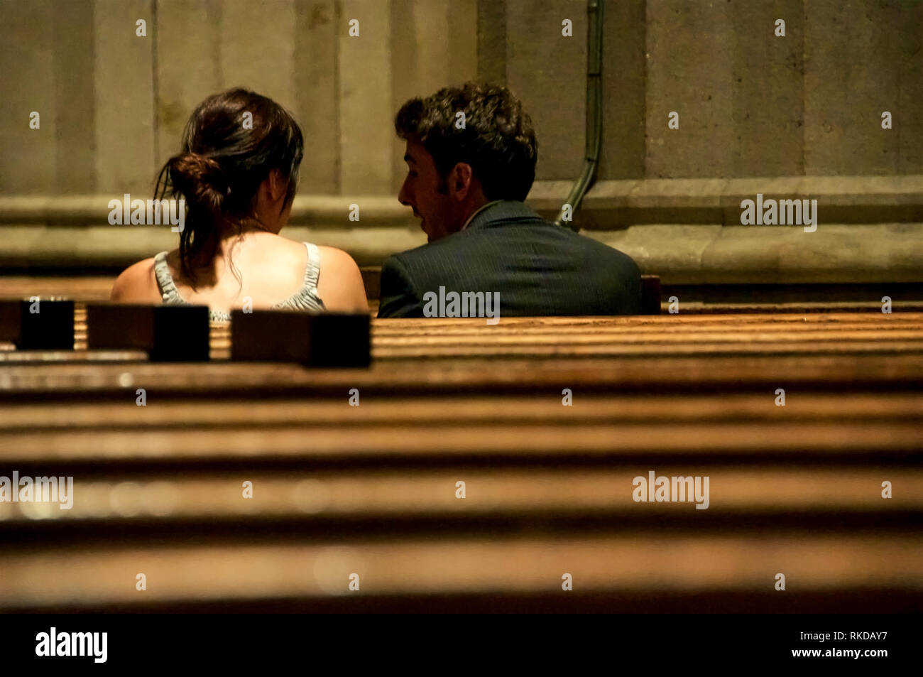 Ein Mann und eine Frau drängten sich und verharrten in einem stillen Gespräch zwischen Kirchenbänken. Stockfoto