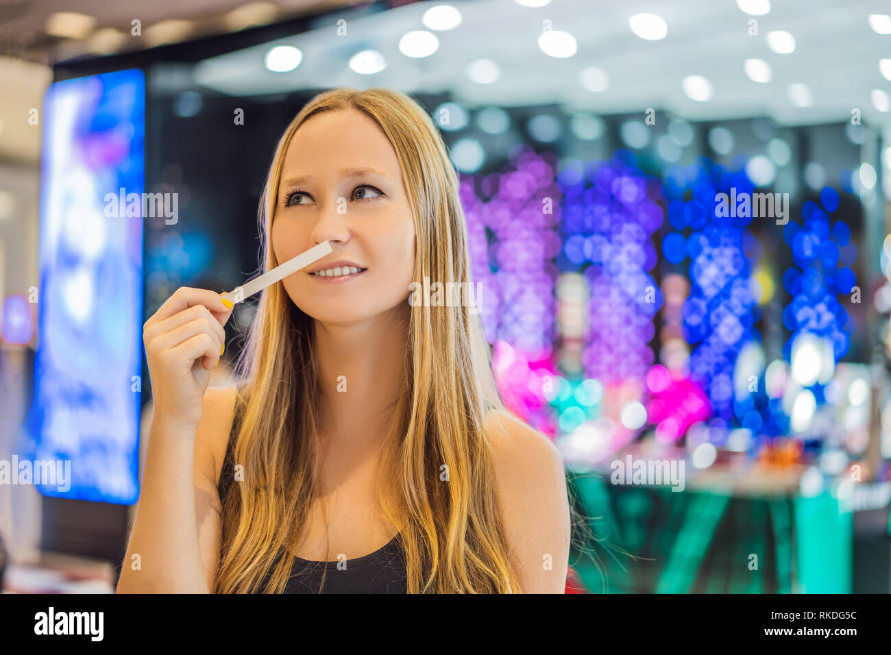 Eine Frau mit Papierstreifen in den Händen hört auf den Duft in der Mall. Stockfoto