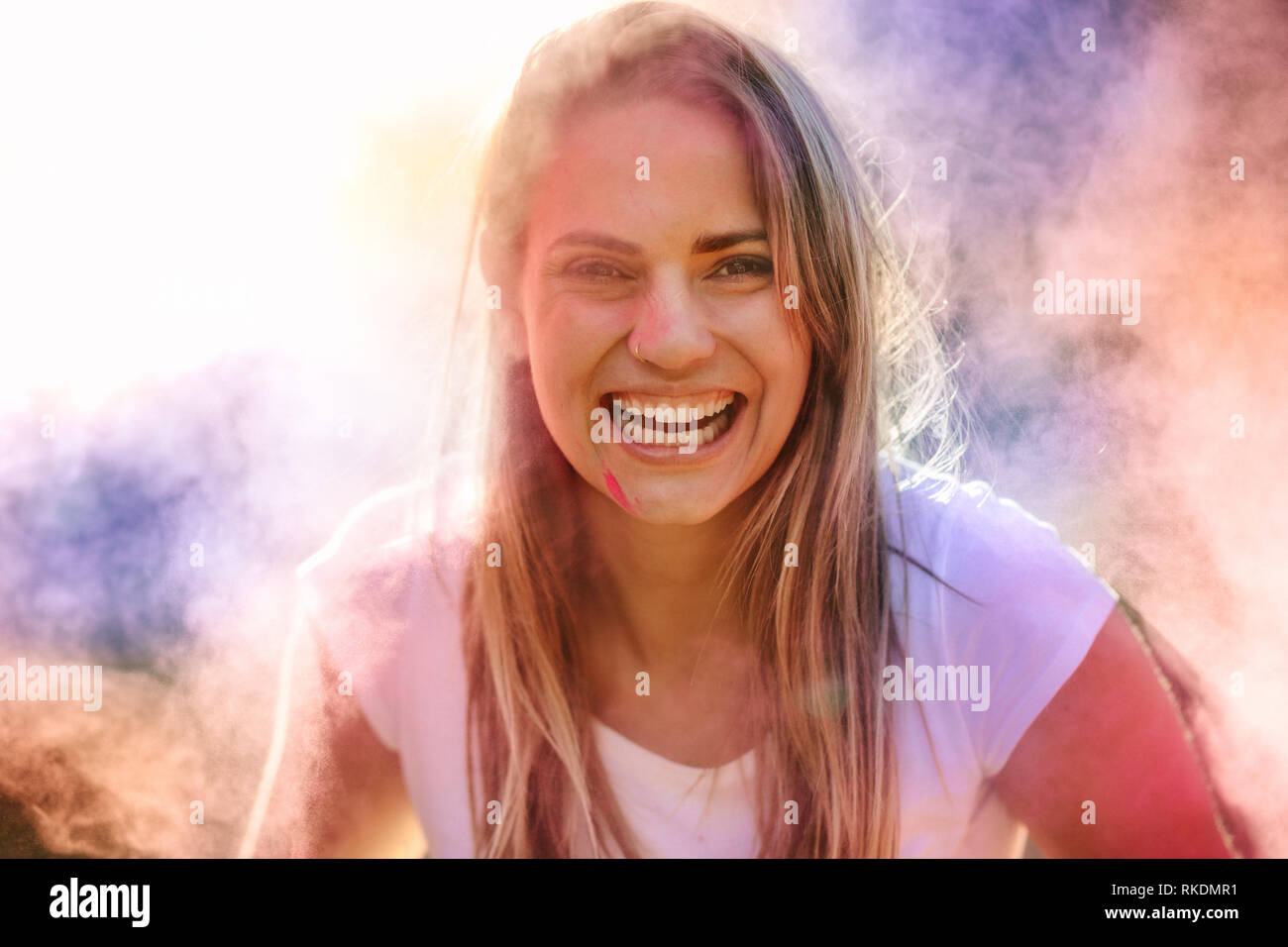 Lächelnde Frau spielen Holi im Freien mit Puder Farben. Frau Spaß holi Spielen mit Farbe Pulver in der Luft im Hintergrund, kann der Verletzte erblinden. Stockfoto
