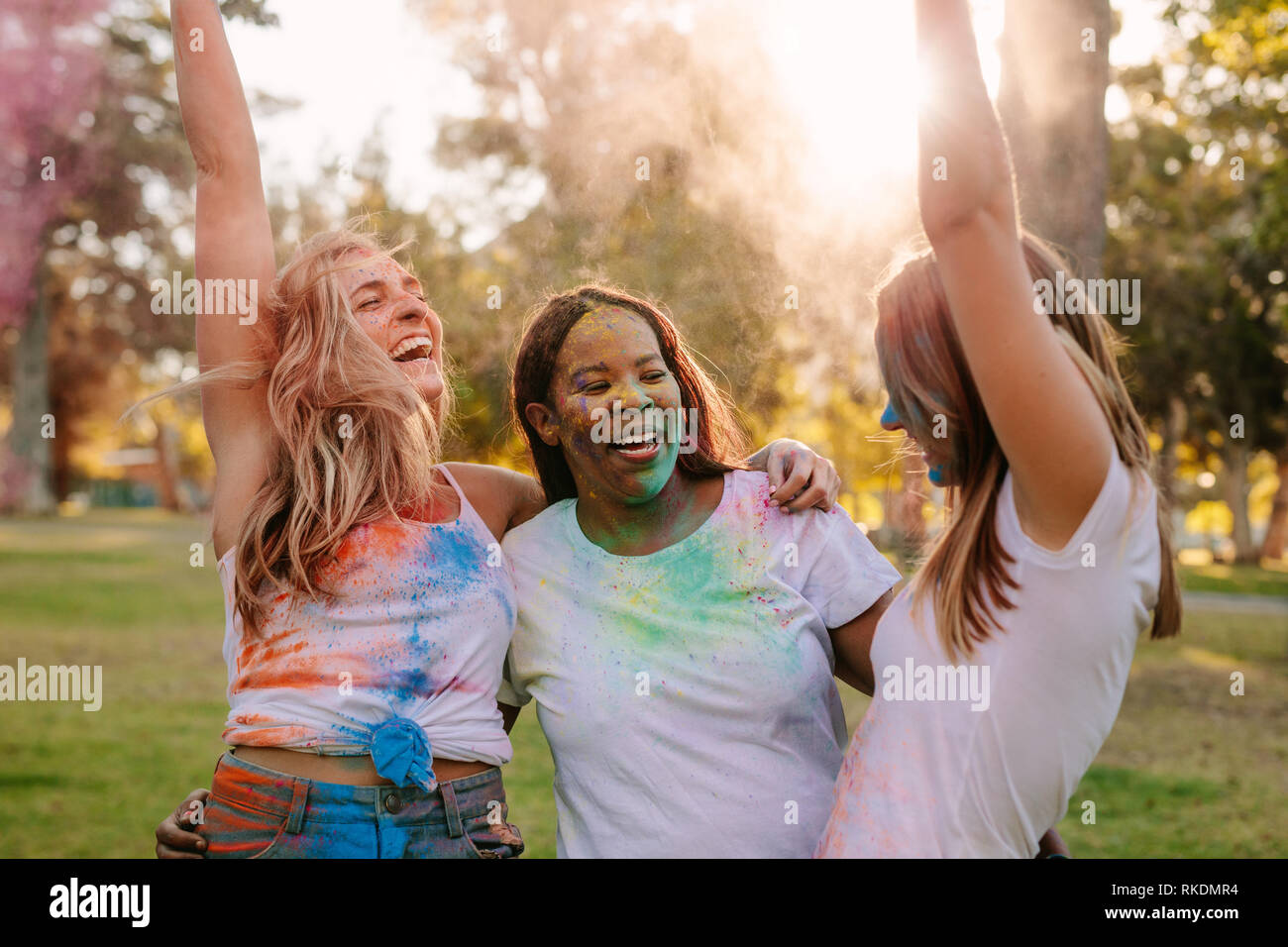 Frauen, die Freunde genießen Holi mit Puder Farben und Tanz in der Freude. Gruppe von drei Frauen, die Freunde holi Spielen in einem Park. Stockfoto