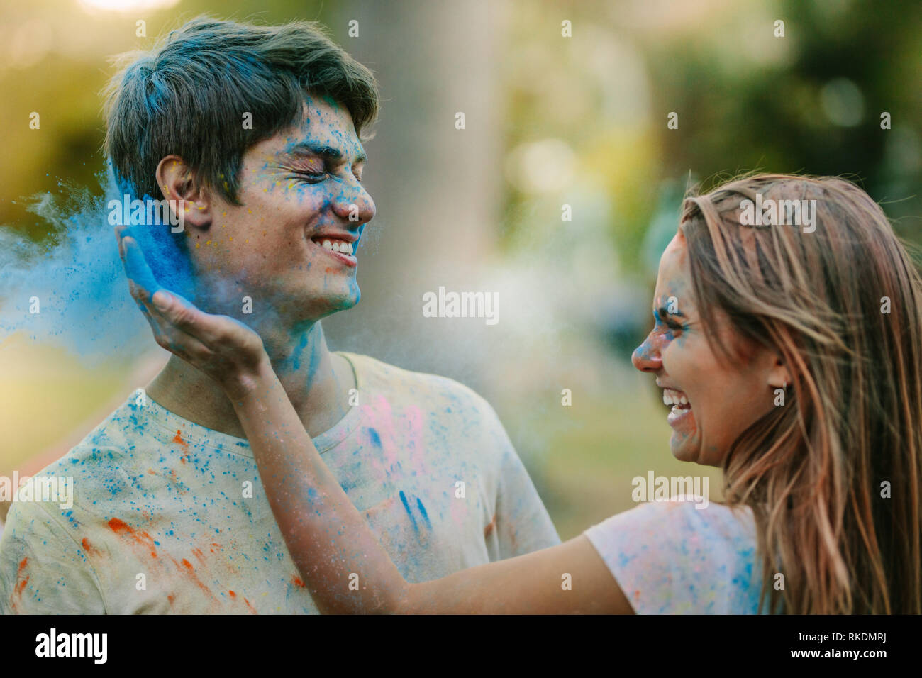 Lächelnde Frau, die Farbe zu einem Mann. Glückliches Paar spielen Holi mit Puder Farben in einem Park. Stockfoto