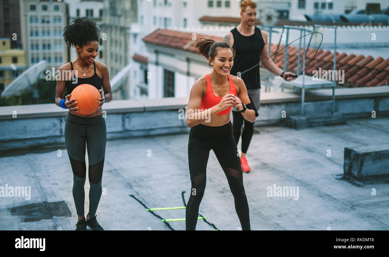 Lächelnd fitness Frauen und ein Mann tun Fitness Training auf der Terrasse. Mann tun Trainings mit Springseil, während seine weiblichen Kollegen Training mit Agi Stockfoto