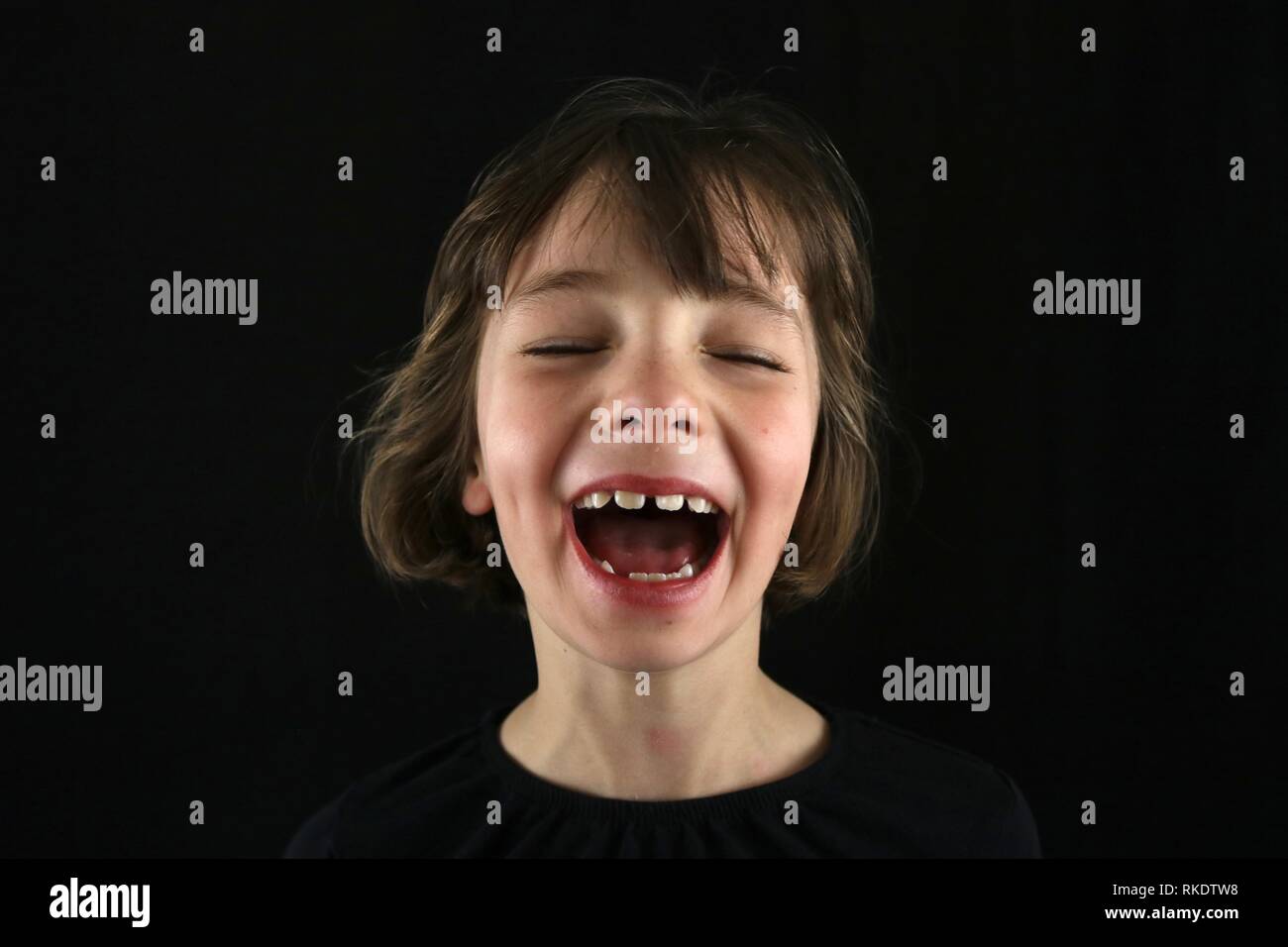 Porträt eines jungen Mädchens laut lachend mit Grübchen und ihre Augen vor einem schwarzen Hintergrund geschlossen Stockfoto