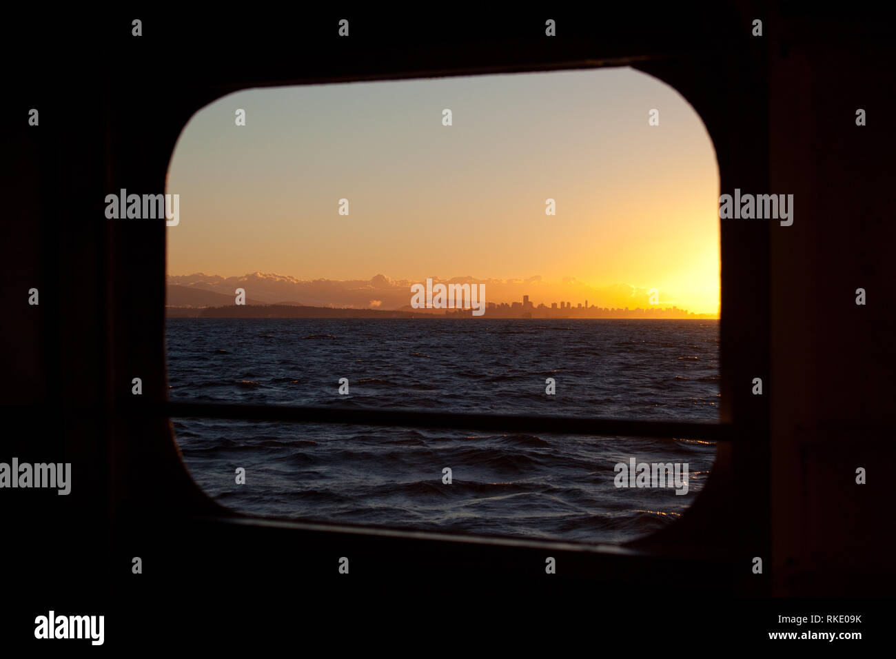 Blick auf die Vancouver City Skyline bei Sonnenaufgang mit Hintergrund Wolken vor der Küste durch ein Bullauge auf einer Fähre in der Georgia gerade gesehen Stockfoto