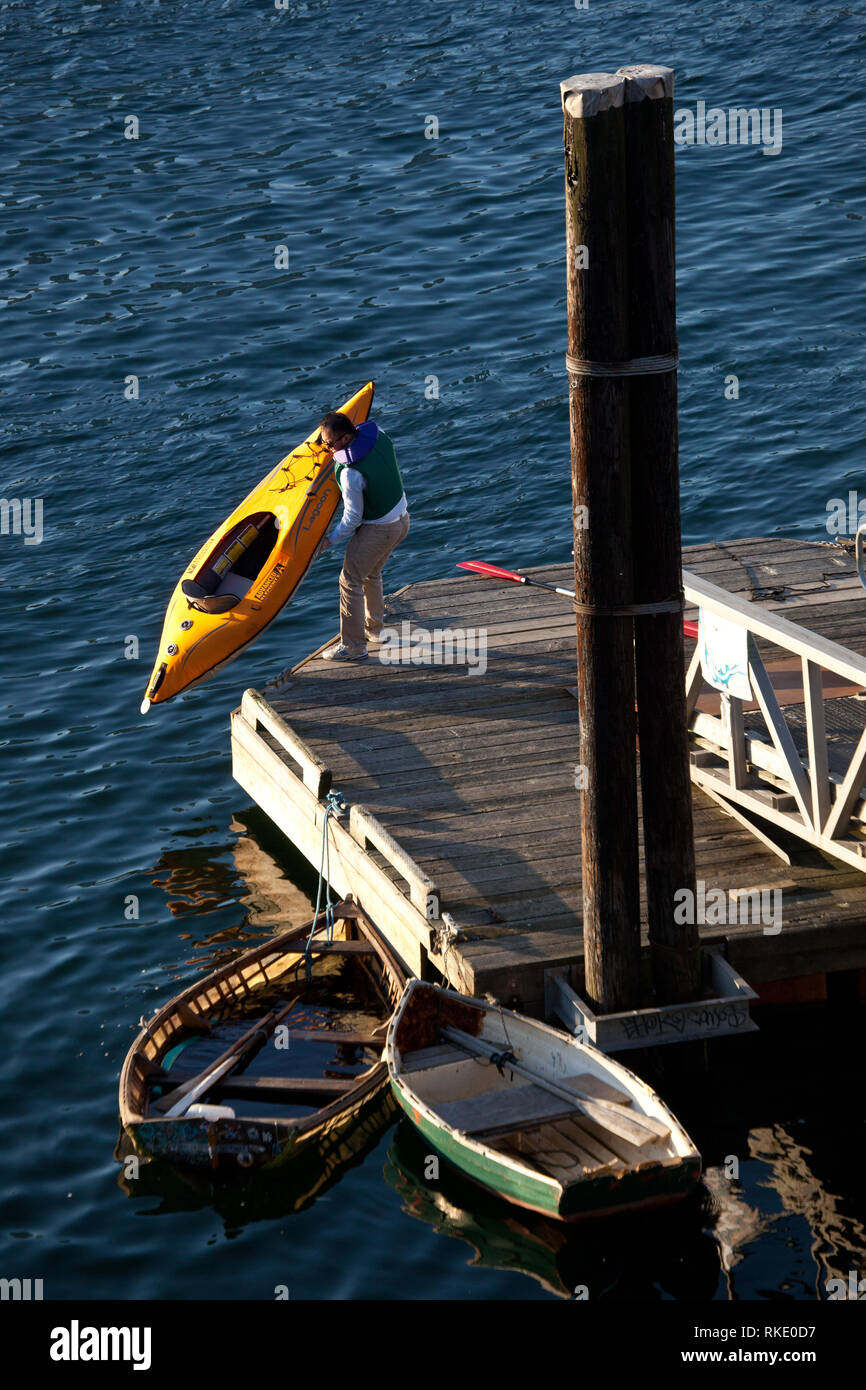 Ein männlicher Paddler tragen ein PFD nimmt seinen gelben Kajak aus dem Hafen heraus bei einem False Creek öffentlichen Dock in Vancouver, British Columbia, Kanada Stockfoto