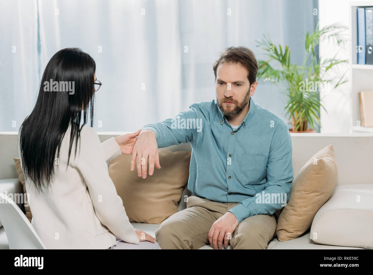 Junge Frau mit Handgelenk der bärtige Mann sitzt auf der Couch während der Hypnotherapie Stockfoto