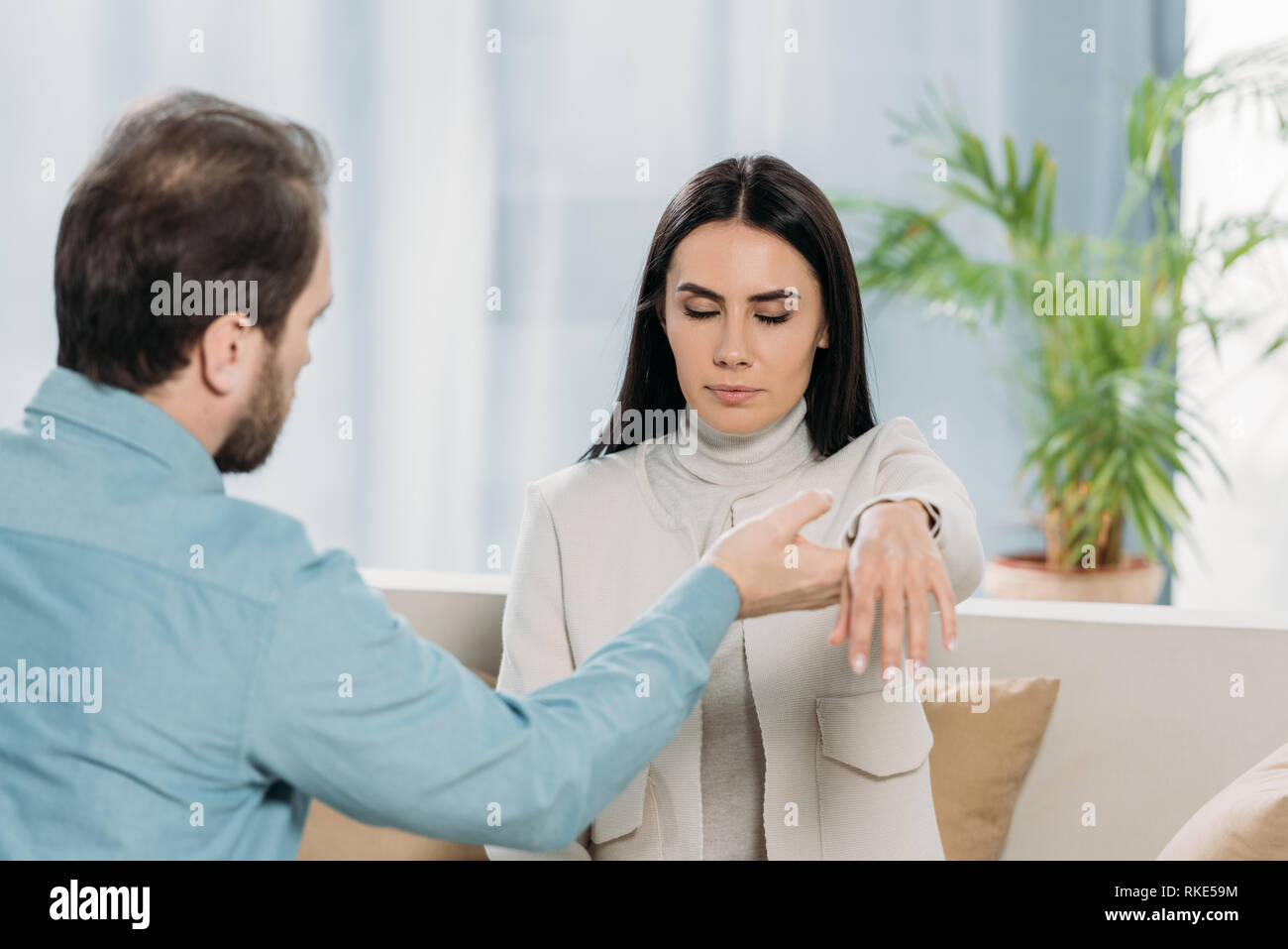 Bärtige Hypnotiseur holding Handgelenk der jungen Frau mit geschlossenen Augen während der Hypnotherapie Stockfoto