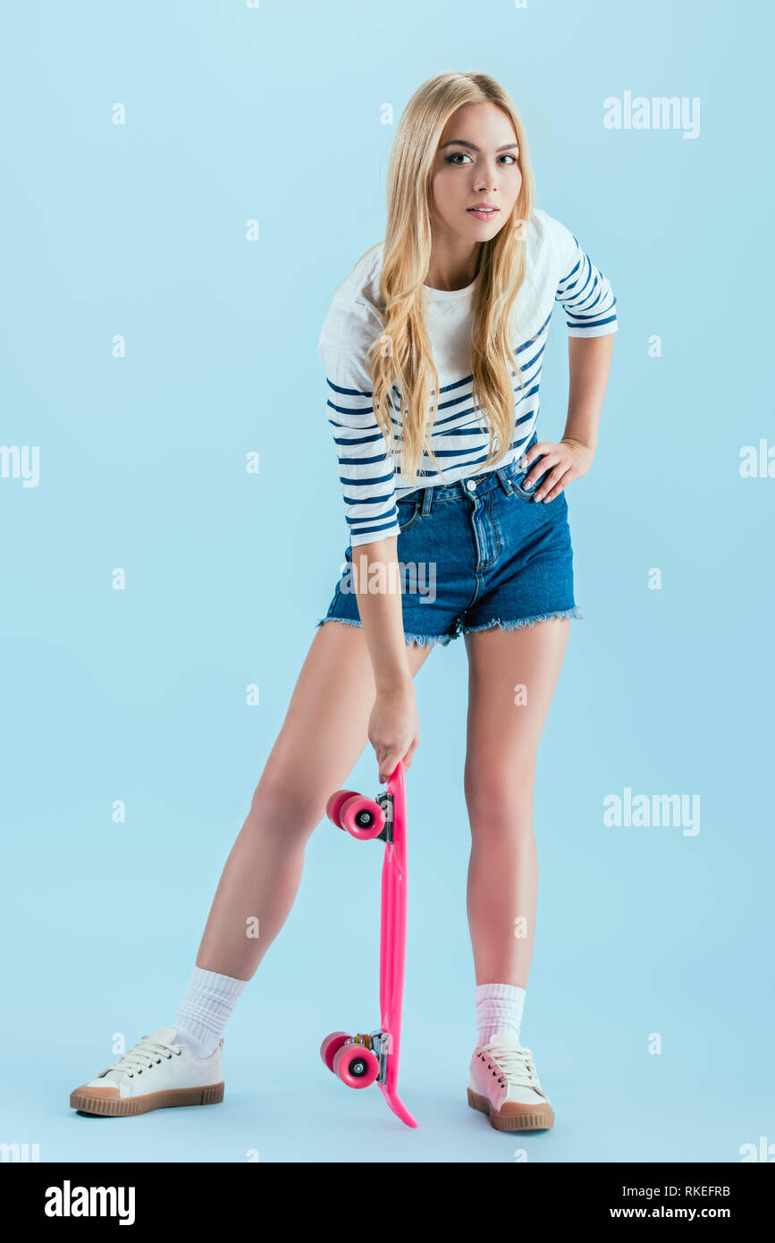 Charmante blonde Mädchen mit rosa Longboard isoliert auf Blue posiert Stockfoto