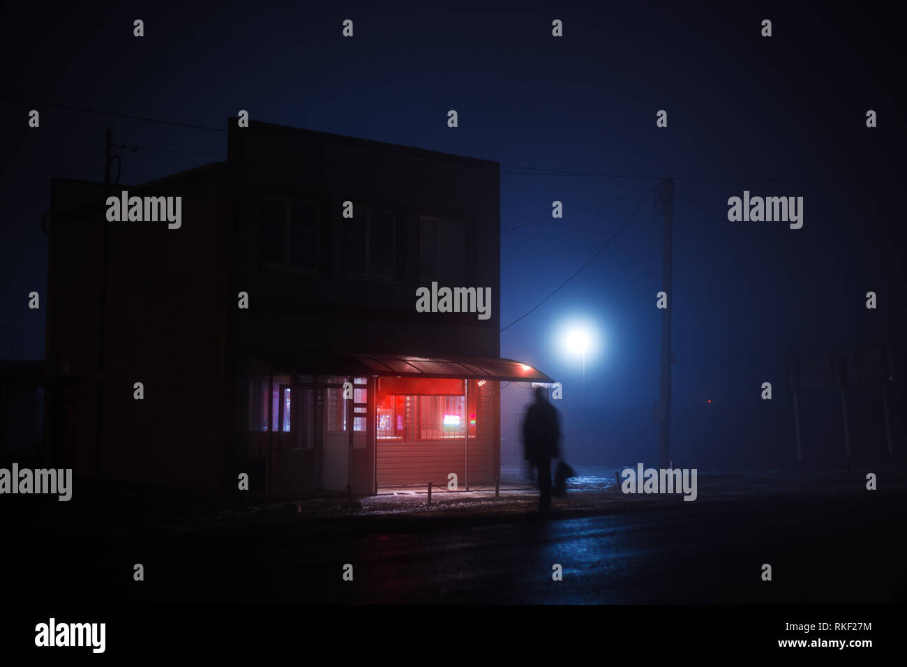 Nacht blau nebligen Landschaft. Ein kleiner Laden mit einem rot beleuchtet Namensschild steht auf der Seite der Straße, eine schmierige Silhouette eines Mannes kreuzt die Stockfoto