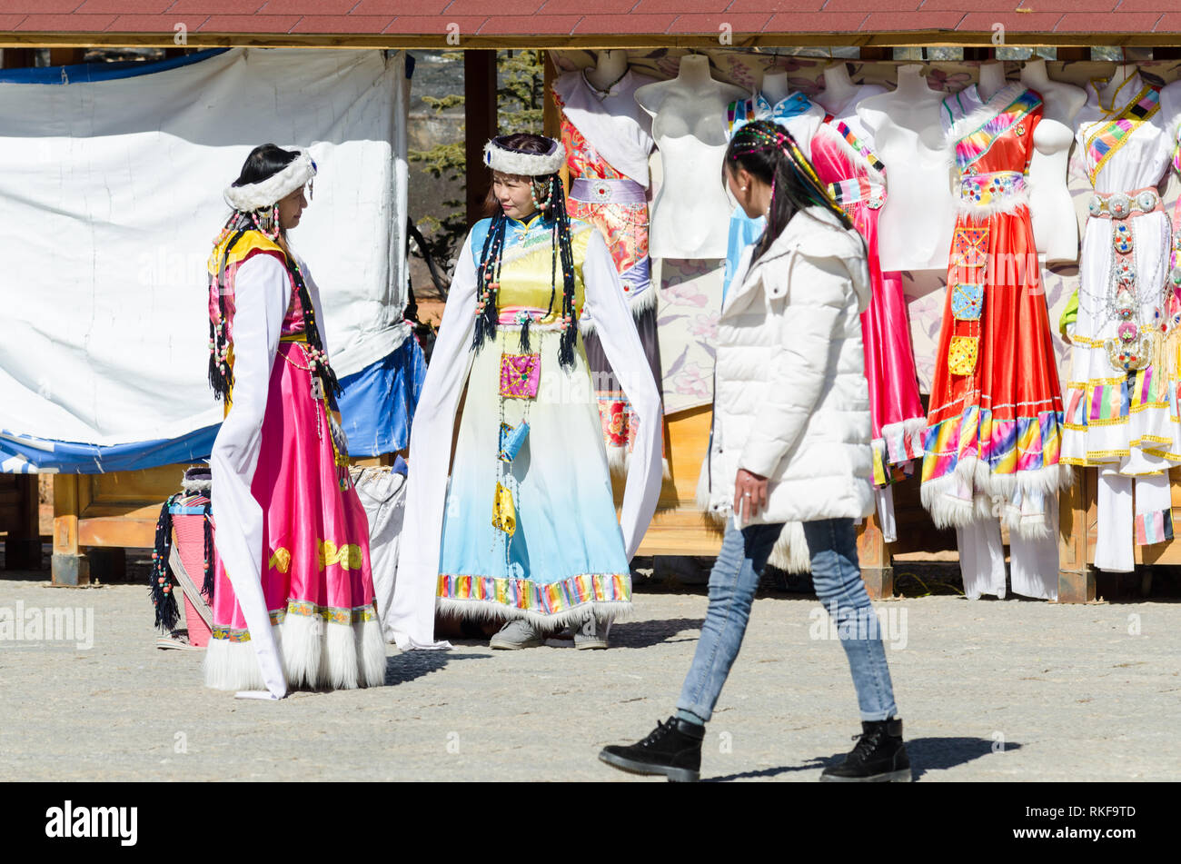 Lokale Mädchen vorbei an zwei Touristen, die traditionelle Kleidung neben Guishan Park, Shangri La, Provinz Yunnan, China Stockfoto