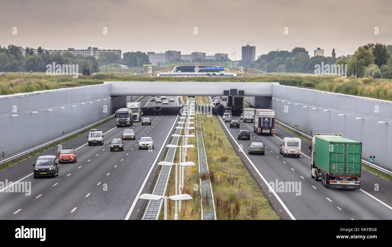 Viel Verkehr auf der Autobahn a4 in der Nähe von Den Haag Gegend Randstad. Autobahn Kreuzung aquaduct Tunnel mit städtischen Gebiet von Rotterdam im Hintergrund, Niederlande. Stockfoto