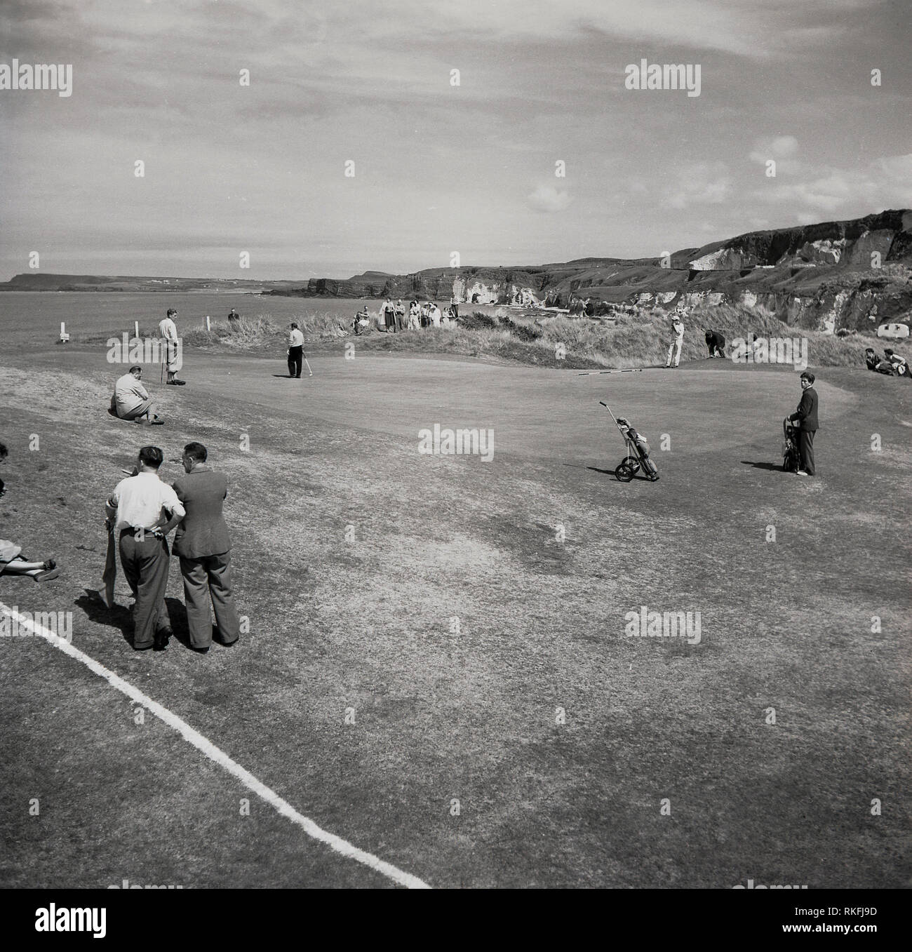 1951, Golfspieler und Caddy mit Flagge auf dem Putting Green auf dem. British Open Golf Meisterschaft, an der Dunluce Links an der Königlichen Portrrush Golf Club, Co Antrim, Nordirland. Der 1888 eröffnete Golfplatz auf der Causeway Coast in Nord Antrim ist durch die 2019 Offene Meisterschaft, der einzige Kurs außerhalb des Festland zum Halten der Veranstaltung zu halten. Stockfoto