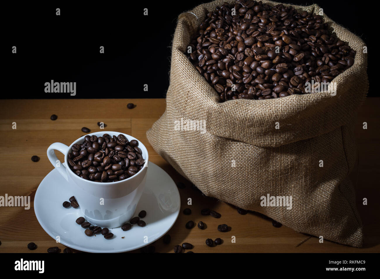 Weiße Tasse mit Kaffee Bohnen und Kaffee Bohnen auf einem hölzernen Oberfläche und auf die weiße Untertasse verstreut gefüllt. Stockfoto