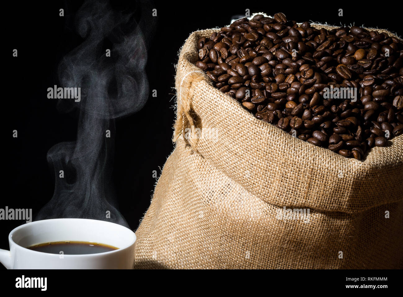 Gebrühten Kaffee in eine weiße Tasse mit Dampf oder Dunst und Kaffeebohnen in einem sackleinen hessische Sack im Hintergrund. Stockfoto
