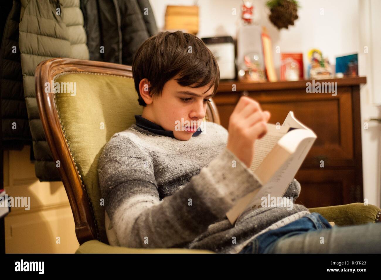 Teenager liest ein Buch im Sessel zu Hause. Stockfoto
