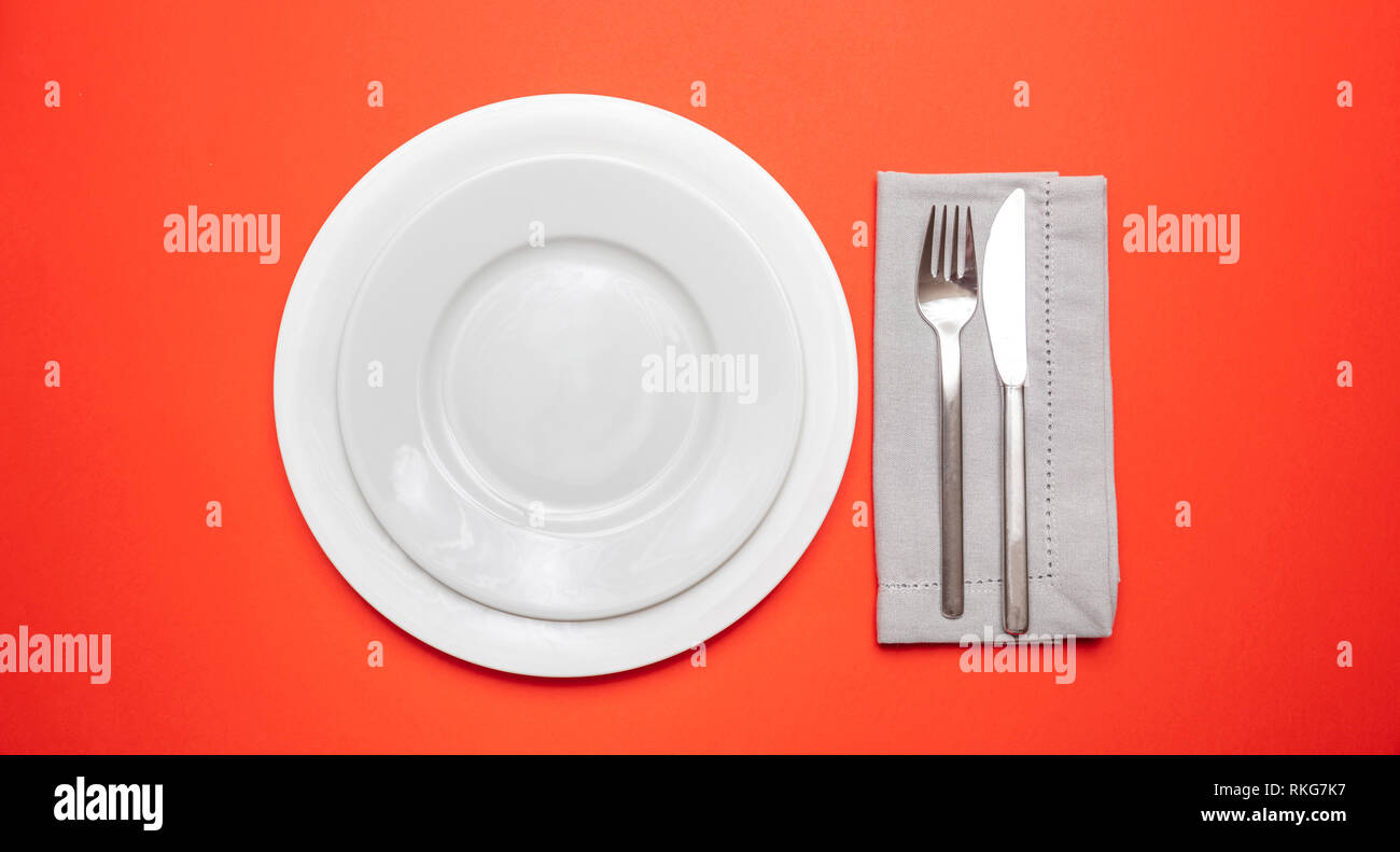 Tabelle setzen, Einstellung auf Rot. Satz von leeren weißen Teller und Besteck auf rot, orange Farbe Hintergrund, Ansicht von oben, kopieren Raum Stockfoto