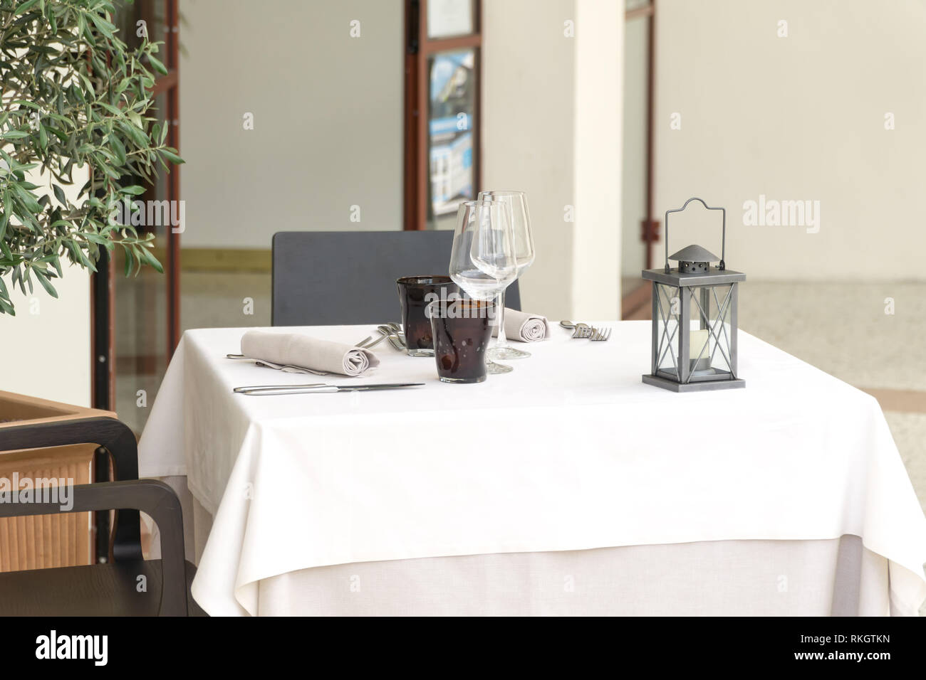 Eine leere Tabelle für Zwei in einem Restaurant, mit einer weißen Tischdecke mit zwei Tisch Sets und eine Laterne bedeckt, in einem Café oder Restaurant außerhalb. Stockfoto