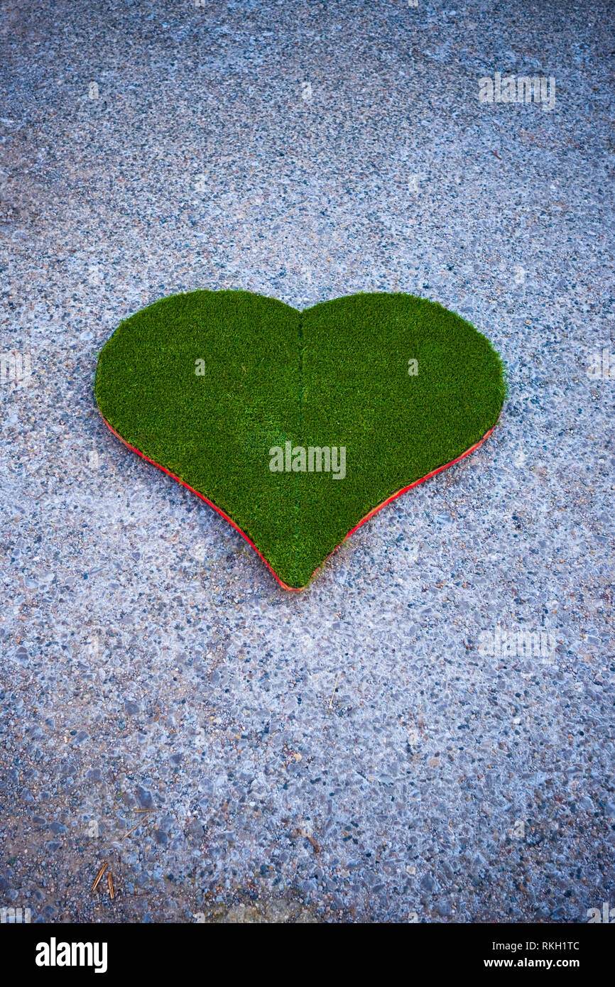 Ein Ausschnitt, der das Herz aus Kunststoff grün Gras an Bord liegt an einer Straße mit Kies Stockfoto