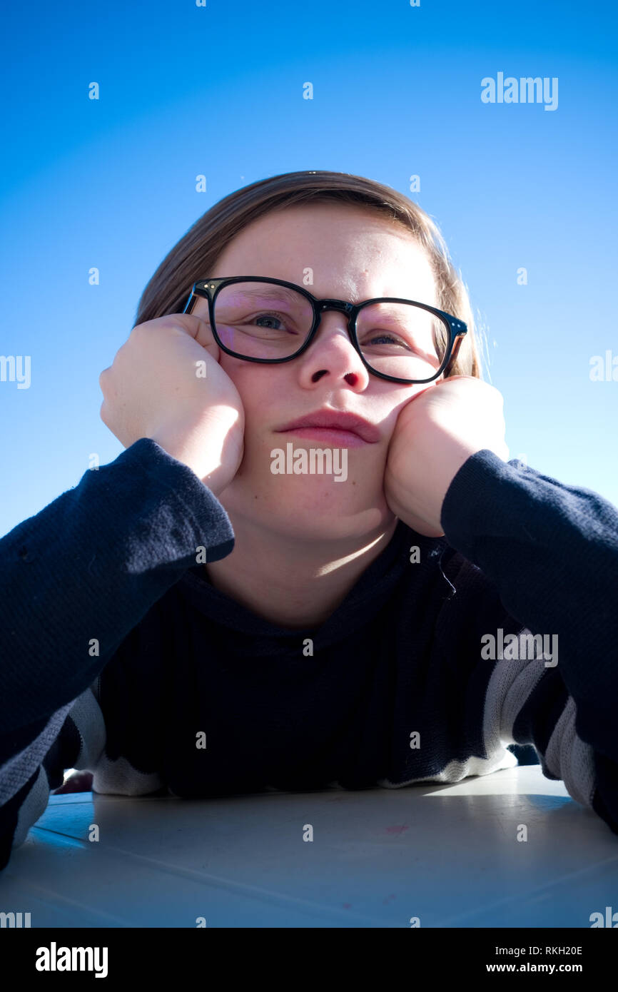 Nahaufnahme eines sitzen elf Jahre alten Jungen mit Brille sein Gesicht in seinen Händen ruht, während Tief in Gedanken und Suchen grumpy Stockfoto