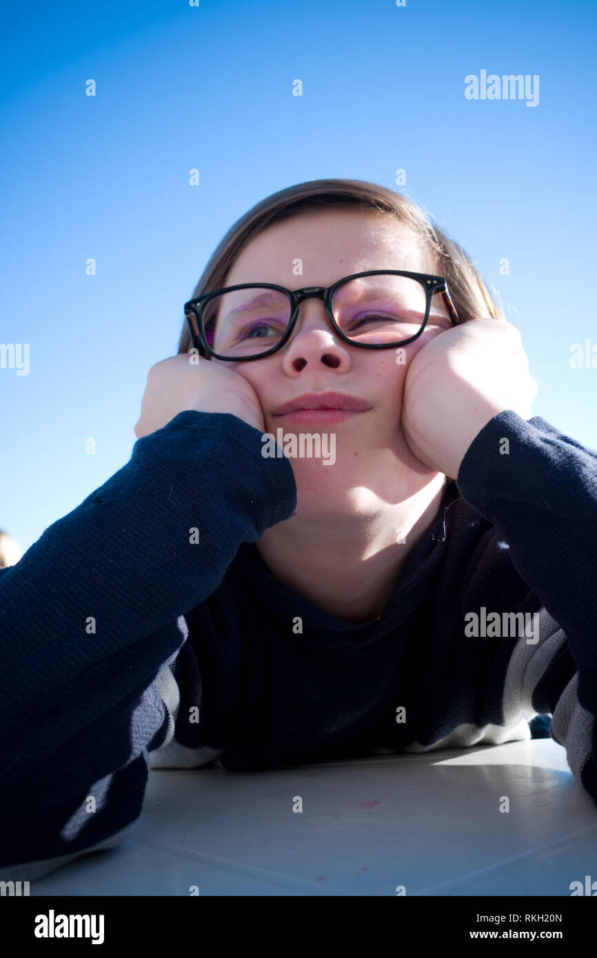 Nahaufnahme eines sitzen elf Jahre alten Jungen mit Brille sein Gesicht in seinen Händen ruht, während Tief in Gedanken und Suchen grumpy Stockfoto