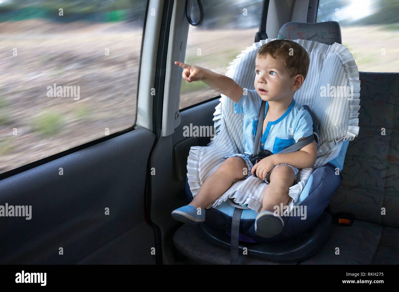 Cute little boy beobachten die Landschaft von seinem Auto Kindersitz. Er zeigt etwas. Stockfoto