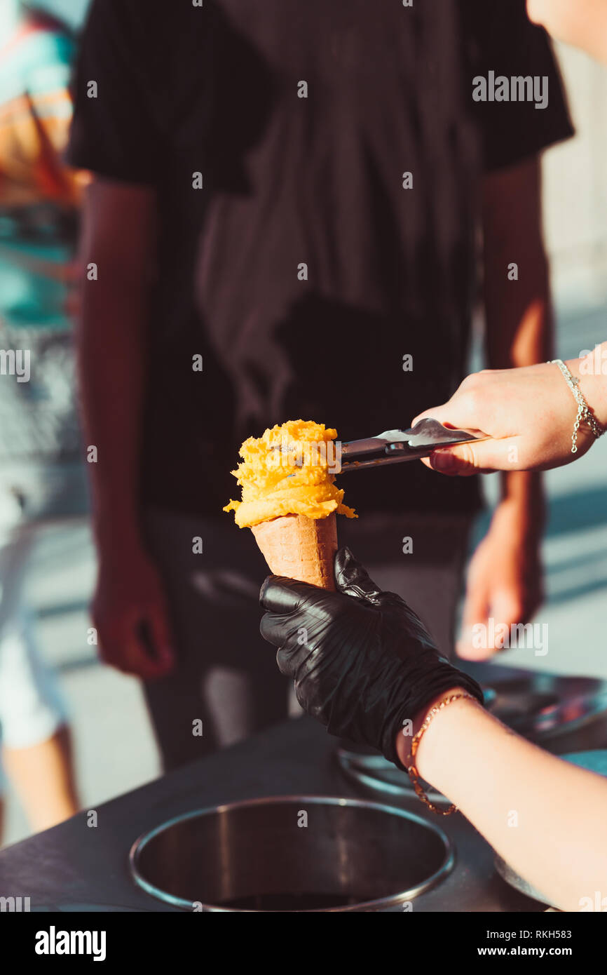 Junge kaufen Eis in einem Candy Shop durch eine Straße. Frau setzen eine Kugel gelb Icecream, der mit einem Kegel Stockfoto