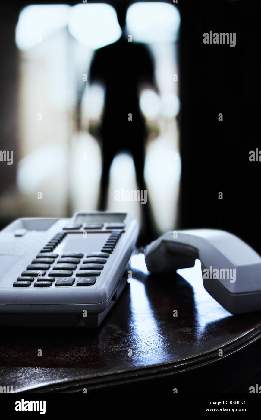 Im Vordergrund der Telefonhörer ist aus dem Schneider. Im Hintergrund gegen das Licht, die Silhouette vor der Terrassentür, oder ein Eindringling Stockfoto
