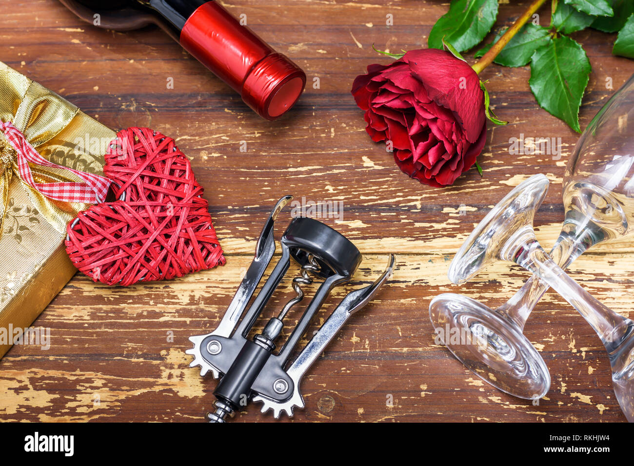 Valentinstag Konzept. Flasche Wein, korbweide Herz, Geschenkbox, rote Rosen, Korkenzieher und Gläser Wein auf hölzernen Tafel. Stockfoto