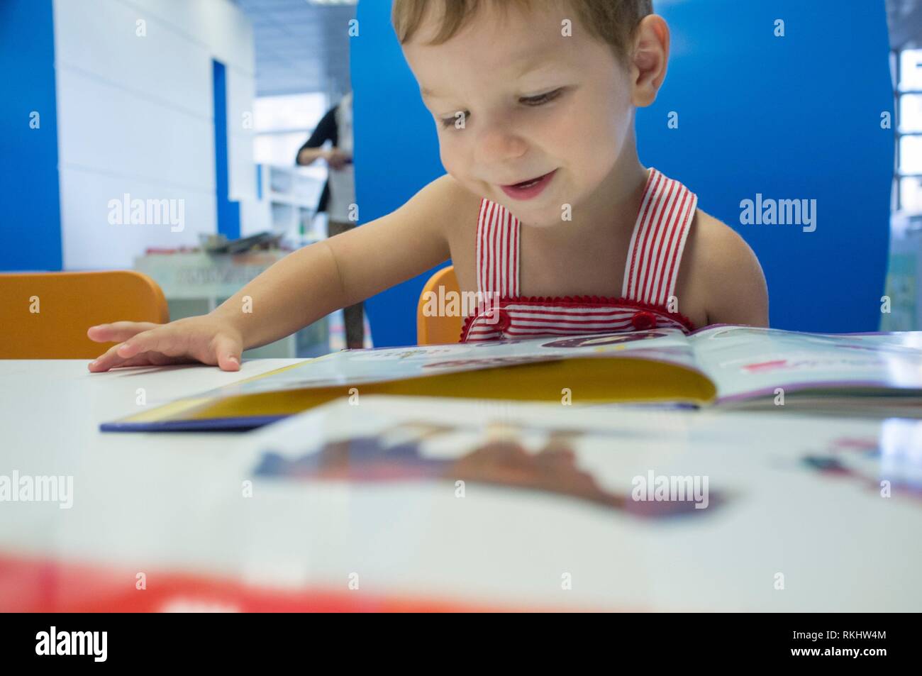 Adorable 2 Jahre Junge surfen Geschichten an der Bibliothek. Genießen Sie die Bücher bei seinem ersten Besuch in der Vorschule Bibliothek. Stockfoto