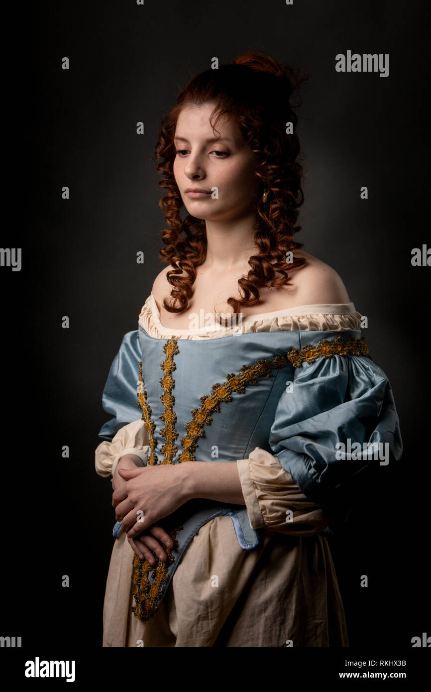 Attraktive junge Dame in wunderschönen barocken Kleid halten die Hände auf Bauch beim Stehen auf schwarzem Hintergrund Stockfoto