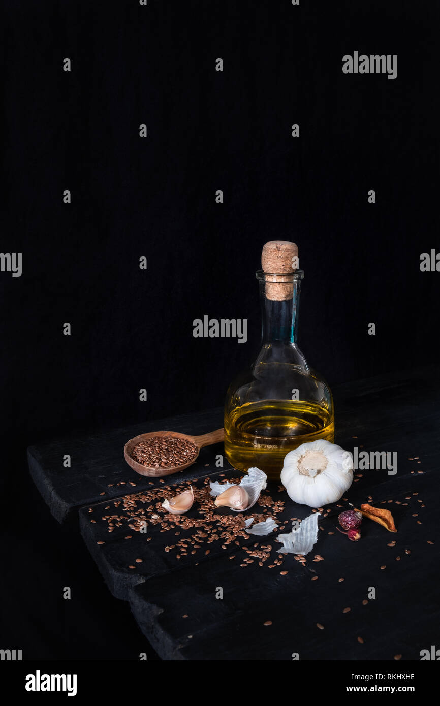 Flasche Olivenöl, Knoblauch und Samen in dunklen rustikalen Hintergrund. Künstlerische Foto von Öl und Kräutern auf alten Schwarzen Tisch Schuß in Low Key ciaroscurro Stil Stockfoto