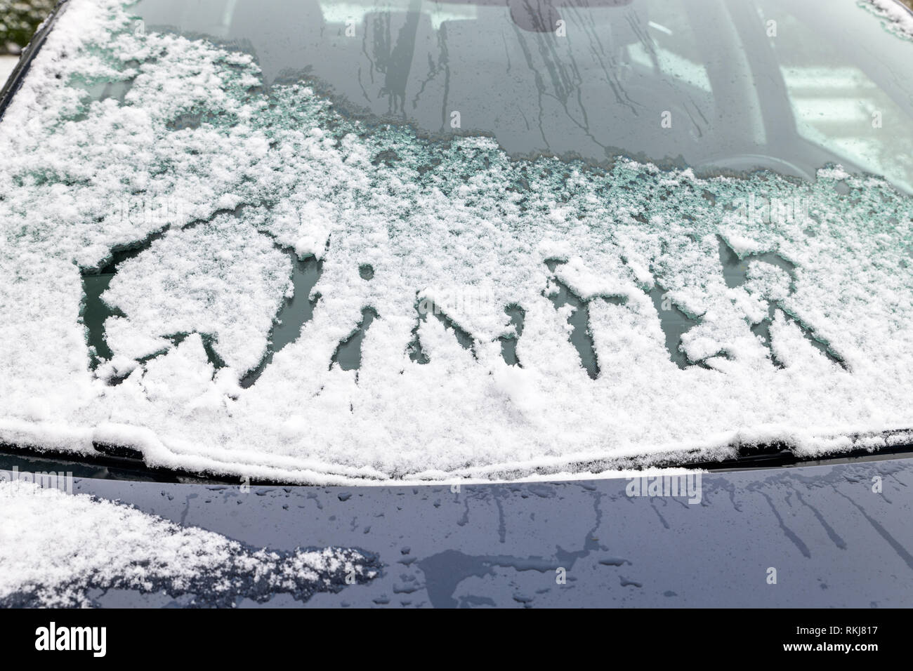 Auto Windschutzscheibe mit Schnee und das Wort Winter im Schnee oberhalb der Scheibenwischer geschrieben. Stockfoto