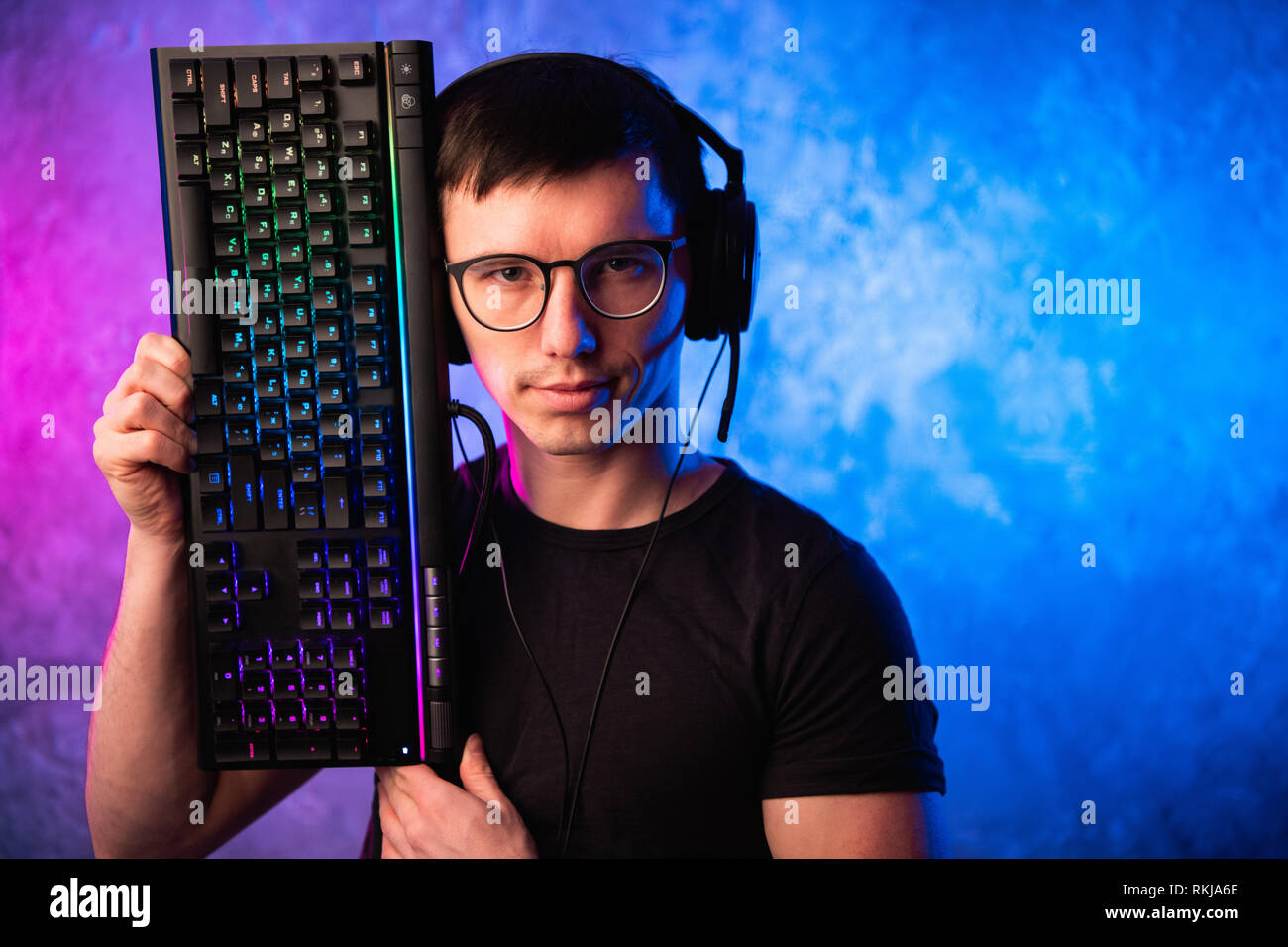 Technologie, Cyberspace, Programmierung und Personen Konzept - Hacker Mann in Headset und Brillen mit Tastatur über Neon Wand Stockfoto