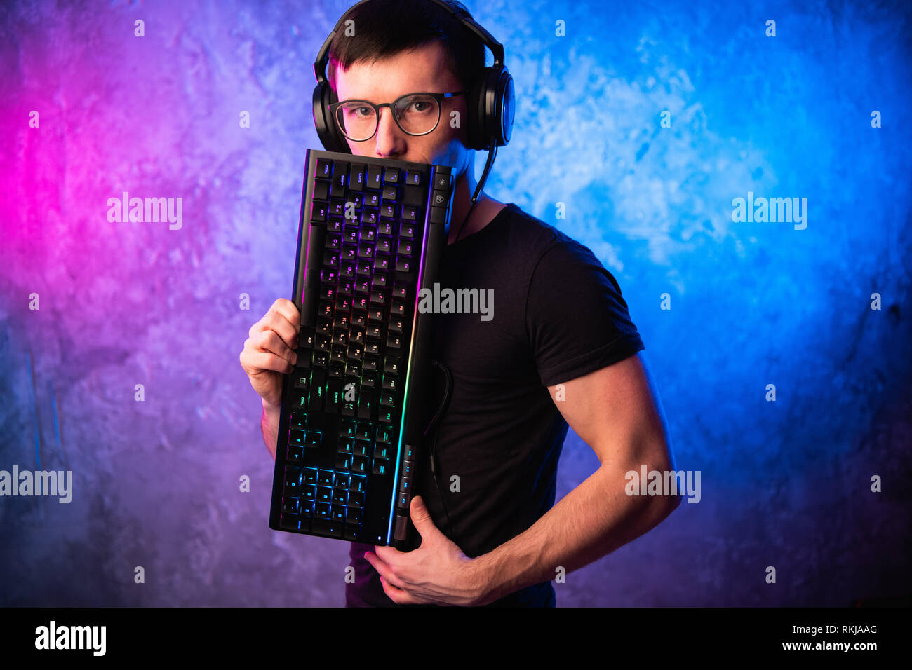 Technologie, Cyberspace, Programmierung und Personen Konzept - Hacker Mann in Headset und Brillen mit Tastatur über Neon Wand Stockfoto