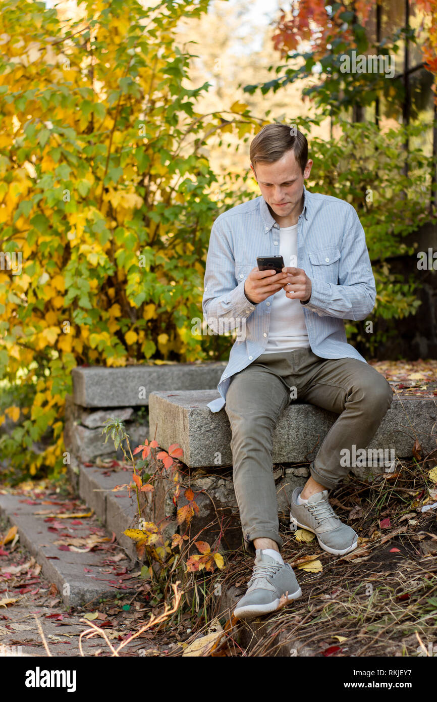 Kerl mit einem Telefon in legere Kleidung im Herbst Park Stockfoto