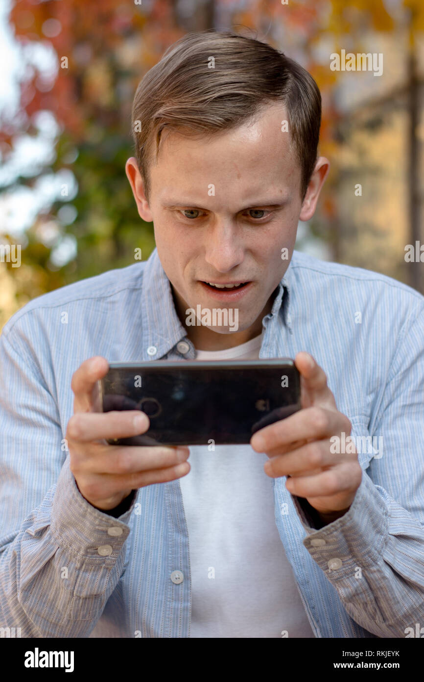 Kerl spielt am Telefon in legere Kleidung im Herbst Park Stockfoto