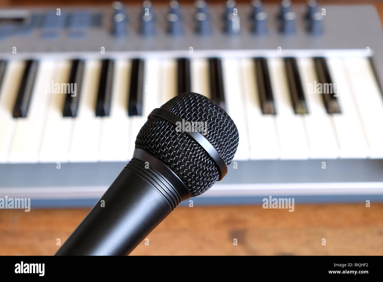 Schwarz vocal Mikrofon nahe gegen Defokussieren elektronische Synthesizer Keyboard mit vielen Reglern in Silber Kunststoff Körper als Hintergrund Stockfoto