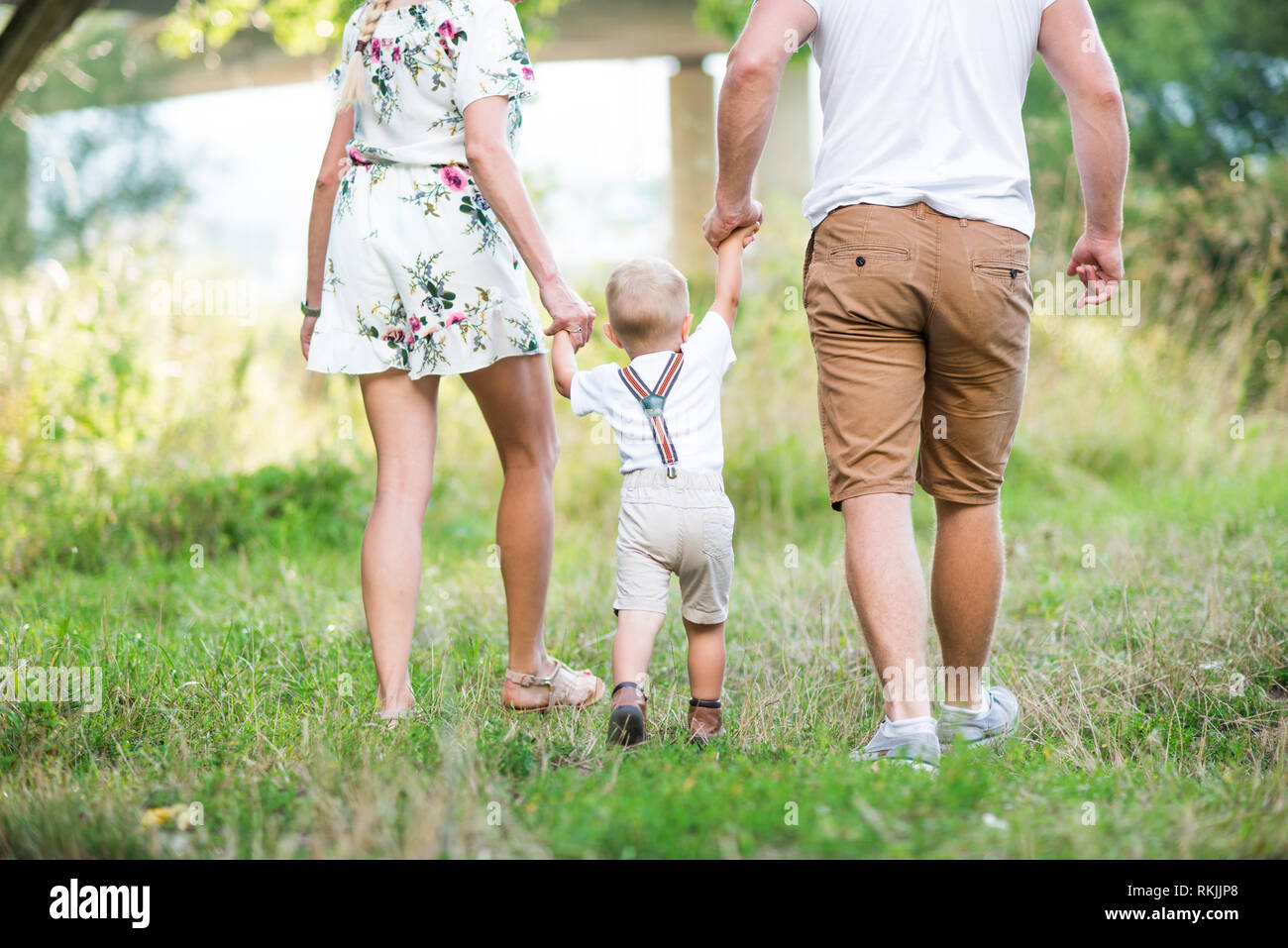 Eine Rückansicht der jungen Familie mit einem kleinen Kind Junge im sonnigen Sommer Natur. Stockfoto