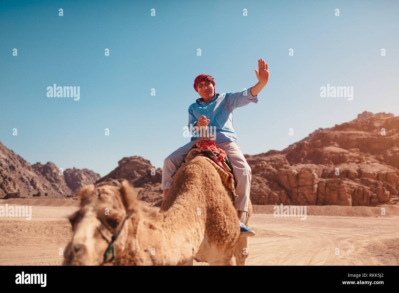 Älterer Mann reitet auf einem Kamel in der Wüste von Sinai Berge. Ihnen gerne touristische winkt für die Kamera. Urlaub in Ägypten Stockfoto Älterer Mann reitet auf einem Kamel in der Wüste von Sinai Berge. Ihnen gerne touristische winkt für die Kamera. Urlaub in Ägypten Stockfoto