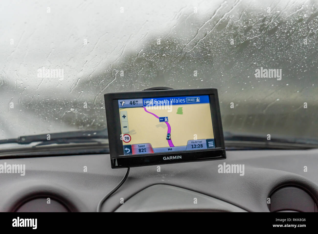 Ein Navigationssystem von Garmin oder Satellitennavigations-/Navigationssystem, das bei regnerischem Wetter in Wales, Großbritannien und Europa an einer Windschutzscheibe des Autos montiert ist Stockfoto