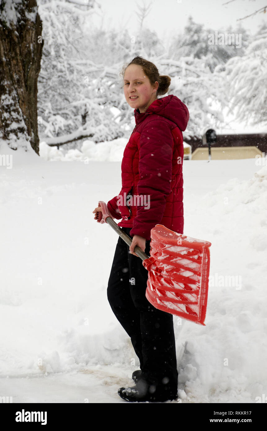 Junge Frau mit einem roten Mantel und Schaufel ist die Reinigung von Schnee Sturm iin Winter, Maine, USA Stockfoto