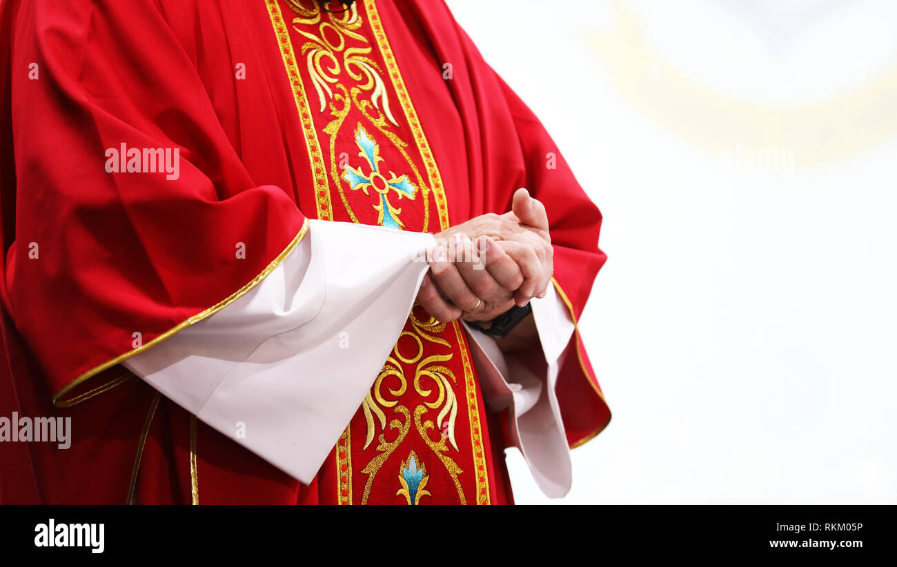 Nahaufnahme von einem katholischen Priester bei der heiligen Messe in der Kirche tragen ein helles rot gold gemusterten parament oder Robe. Mit gefalteten Händen, weißer Hintergrund Stockfoto