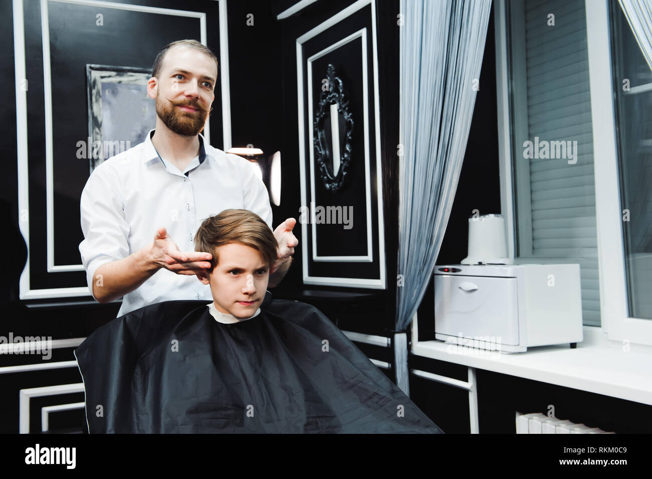 Junge schöne Friseur die Haare schneiden von süßen Jungen im barbershop Stockfoto