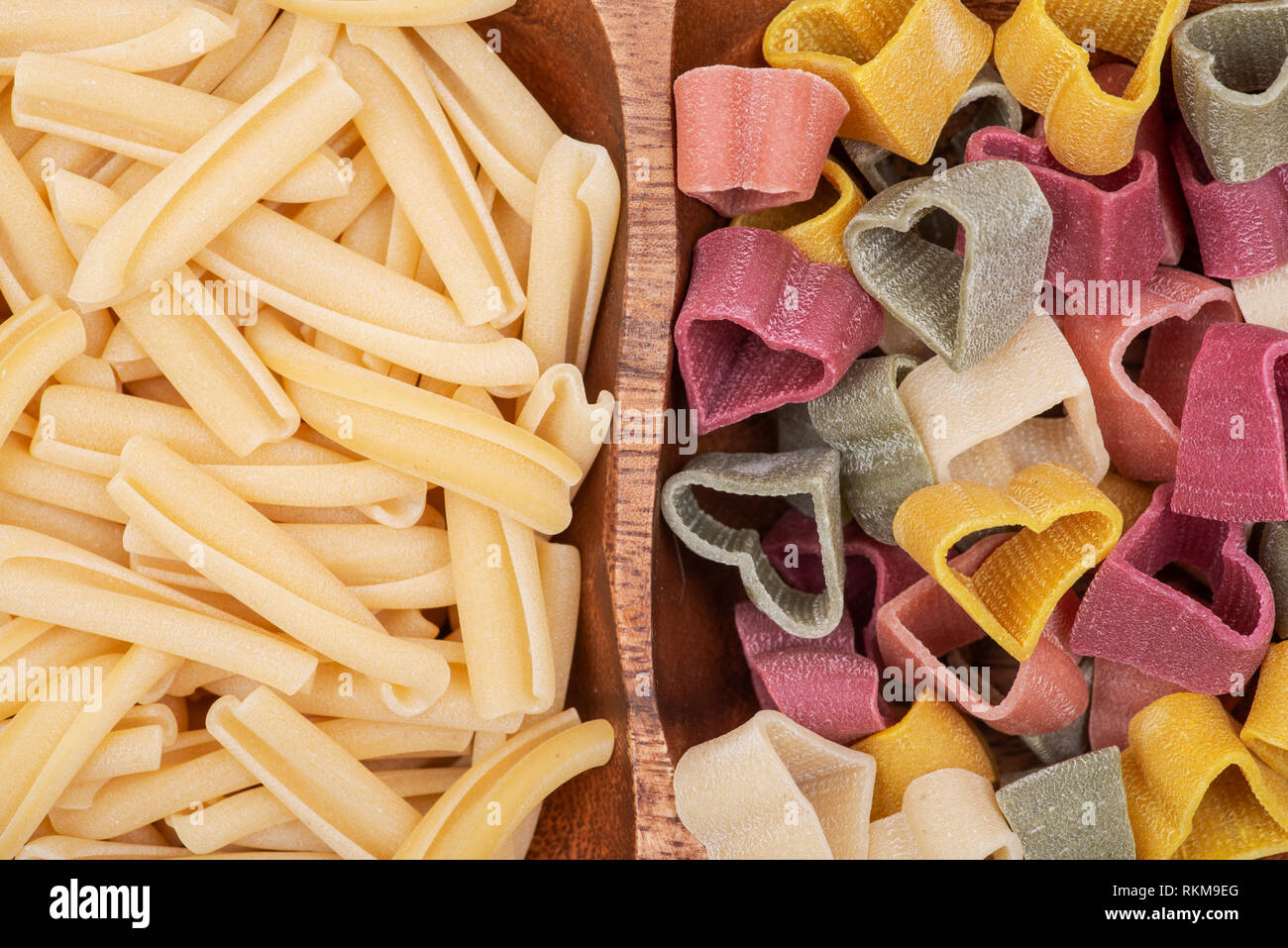 Ungekochte italienische Hartweizengrieß herzförmig und Casarecce Pasta auf eine lange Olivenholz Platte angeordnet sind. Stockfoto