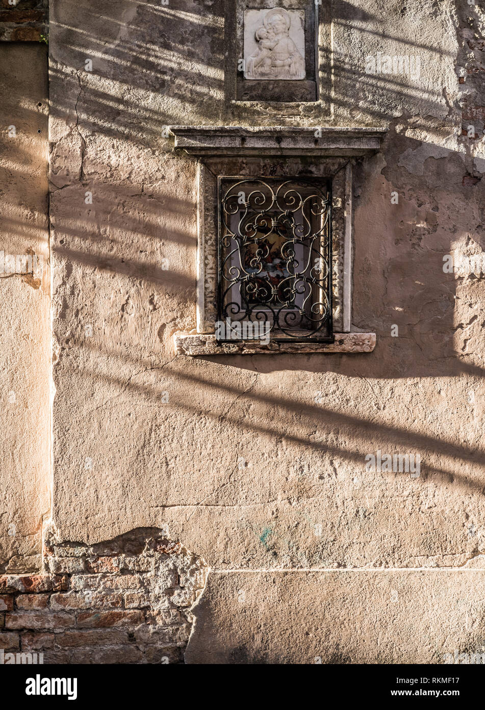 Alte, gesprungene Wand- und Vintage Malerei unter die geschmiedeten Gitter. Sonne und Schatten auf der Wand. Stockfoto
