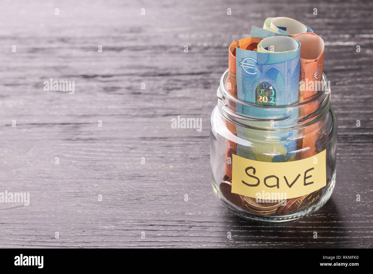 Die Euro-Banknoten und -Münzen in einem Glas auf einem schwarzen Holztisch mit glänzenden Reflexion auf einer glänzenden Oberfläche. Geld sparen Konzept Stockfoto