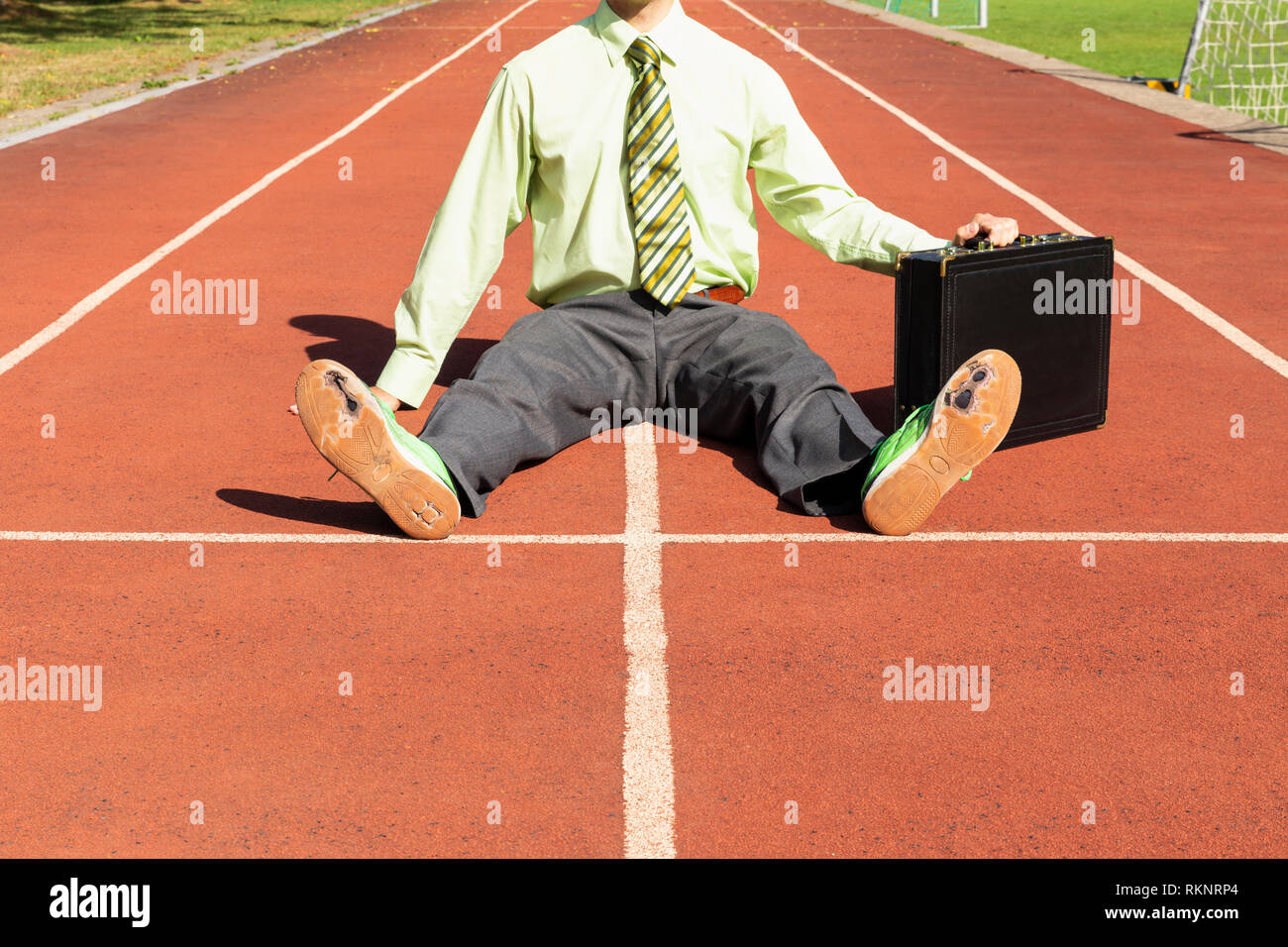 Ein erschöpfter business Mann im grauen Anzug mit grünem Hemd und Krawatte  schwarz Aktenkoffer und gebrochen grüne Schuhe sitzen auf eine Laufstrecke  Stockfotografie - Alamy